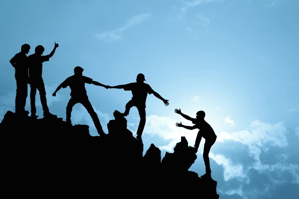 Family climbing up a mountain together with a blue sky and clouds behind them.
